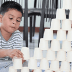 Stacking paper cups into a tall pyramid tower.